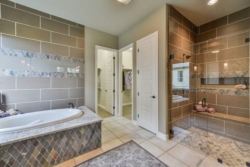 Owners bath featuring warm gray tile and glass shower.