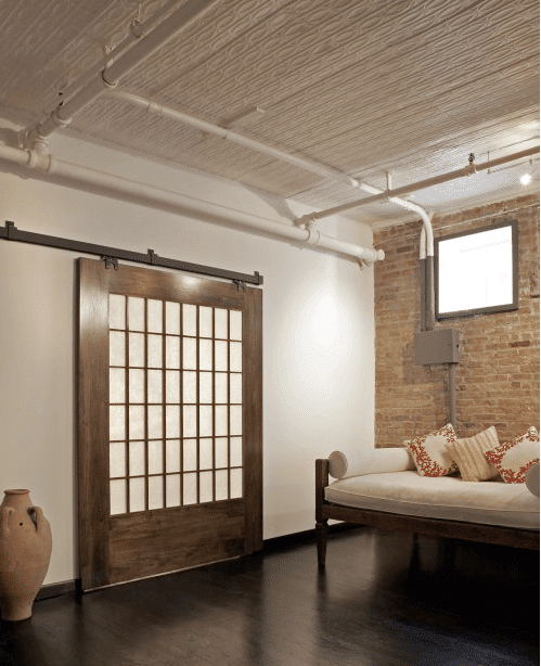 Sliding barn door with exposed pipes on the ceiling.